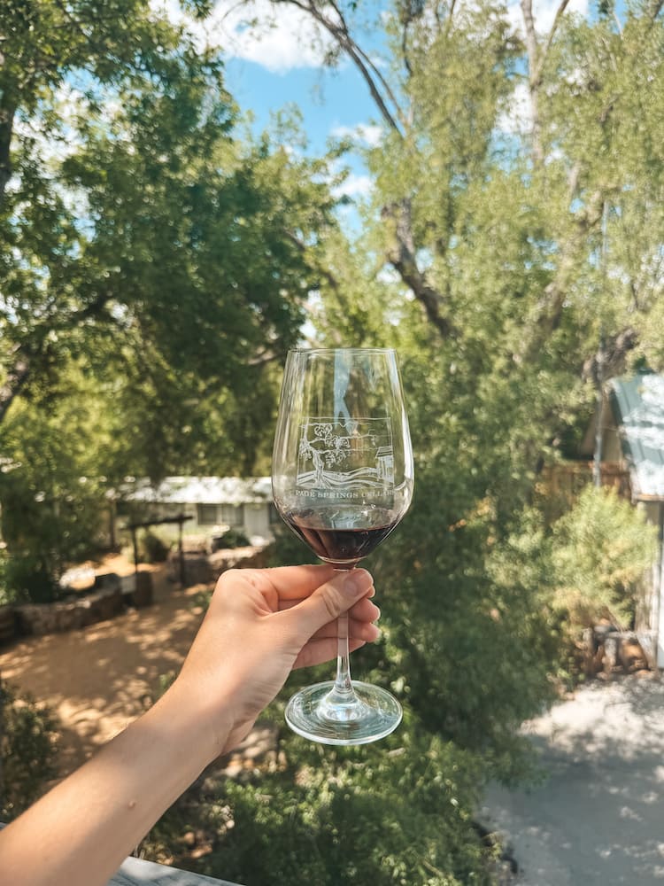 A small glass of red wine in front of trees and greenery at Page Springs Cellars, one of the best wineries in Sedona