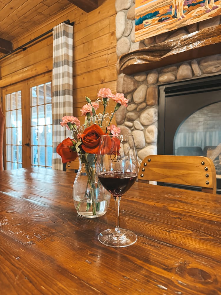 A glass of red wine sitting next to a vase of flowers inside a cozy rustic lodge at one of the best wineries in Sedona
