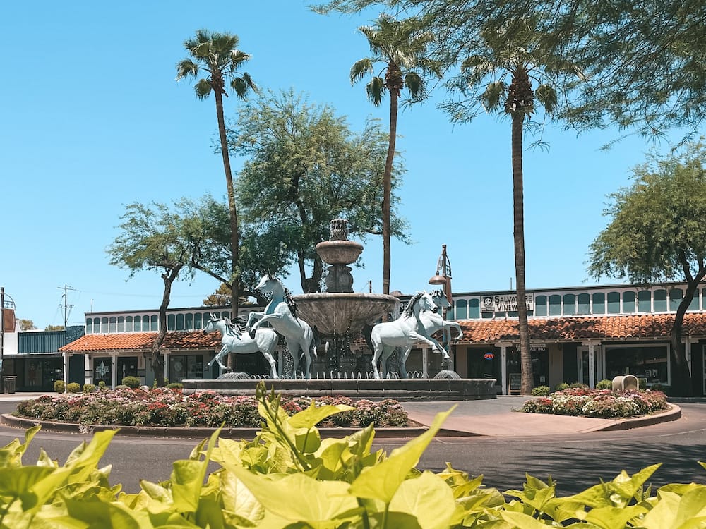 A fountain with blue horses around in with historic buildings and palm trees in the background in Old Town Scottsdale