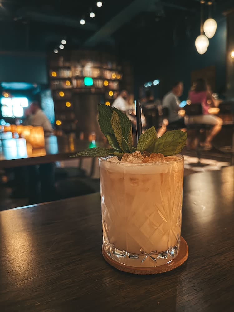 A white cocktail with a leafy garnish in a dimly-lit speakeasy in Scottsdale.