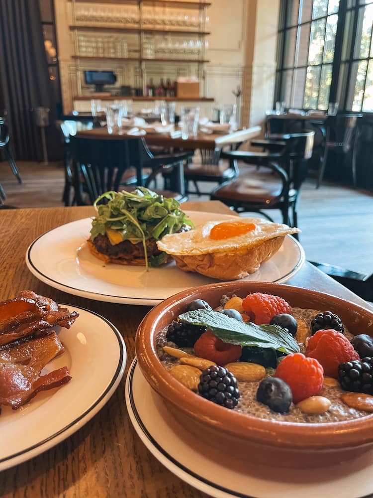 Several plates of food, including a bowl of chis seed pudding topped with berries, nuts, and mint, a plate of bacon, and an egg sandwich, at a restaurant at The Pearl in San Antonio.