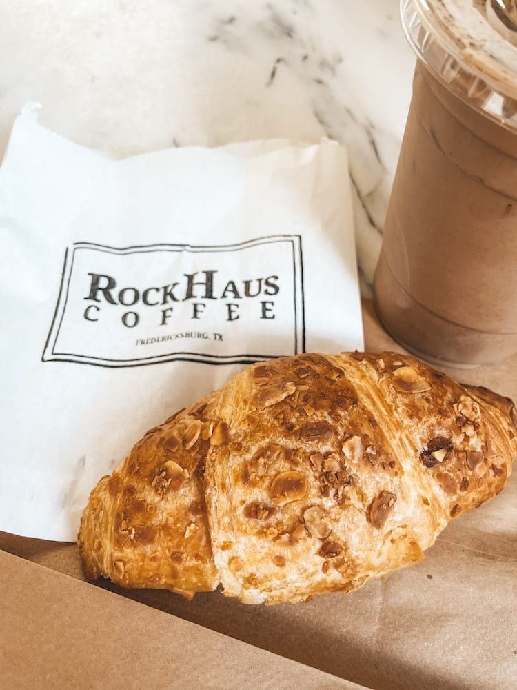 A croissant and iced coffee sitting on a white bag that says RockHaus Coffee on a white marble table