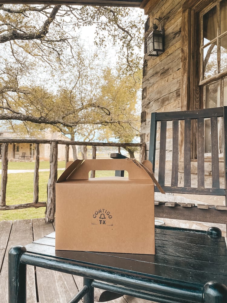 A small cardboard box sitting on a black wood table with trees in the background on a wood porch.