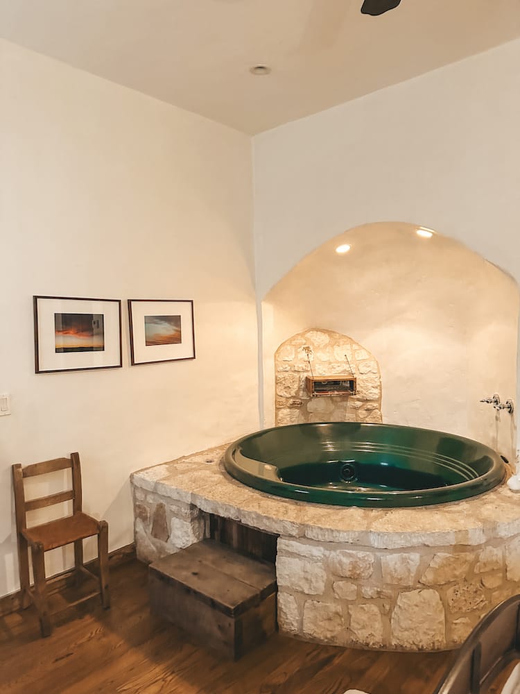 A large green bathtub surrounded by granite rocks in a wood cabin.