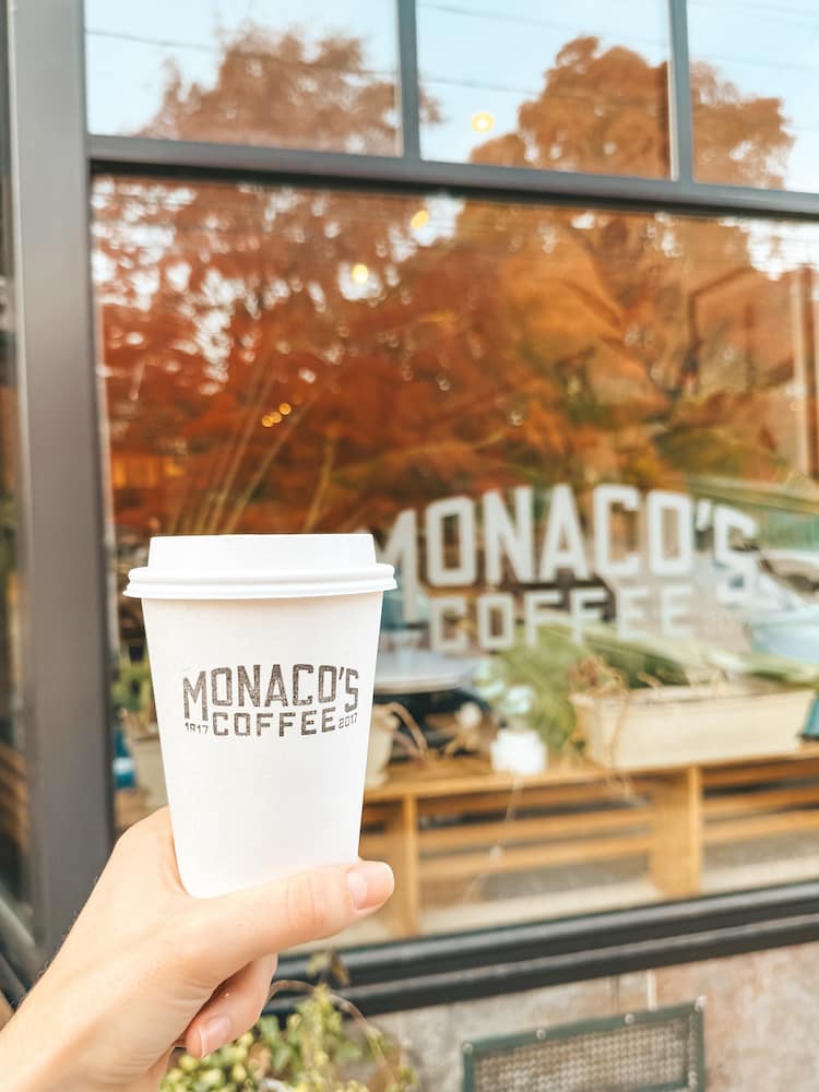 A cup of hot coffee from Monaco's Coffee in front of the storefront for Monaco's Coffee in Downtown Geneva in the Finger Lakes