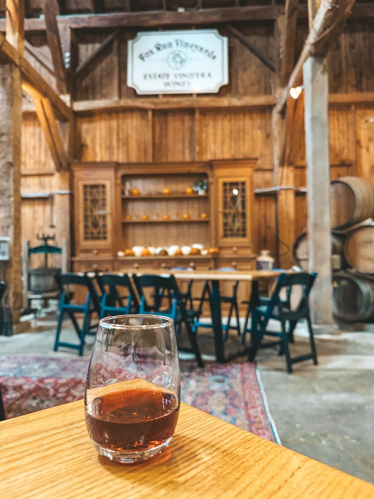 A glass of red wine sitting on a table inside a cozy wooden lodge at one of the best wineries in the Finger Lakes, Fox Run Vineyards