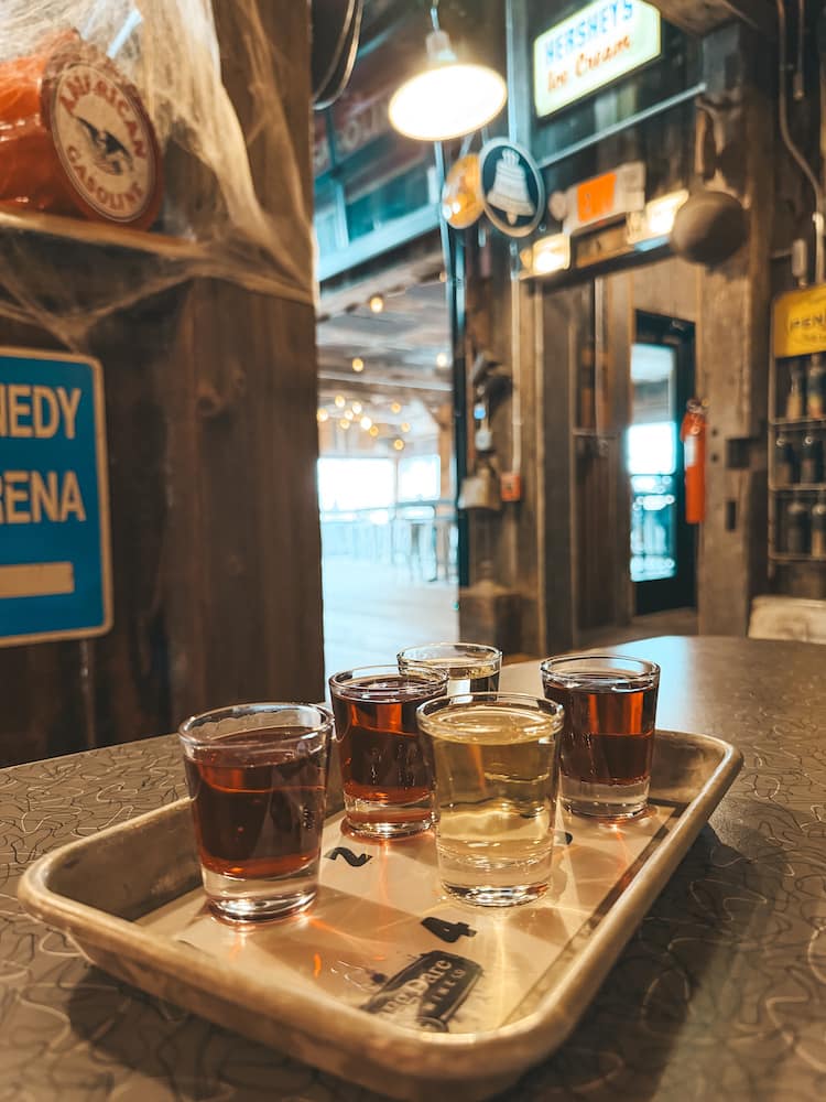 A flight of five white and red wines in shotglasses at Three Brothers Winery In the Finger Lakes with retro decor in the background
