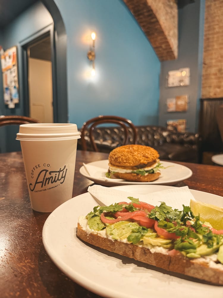A breakfast spread with a cup of coffee, avocado toast, and breakfast sandwich from Amity Coffee in Downtown Penn Yan, one of the best places to stay in the Finger Lakes