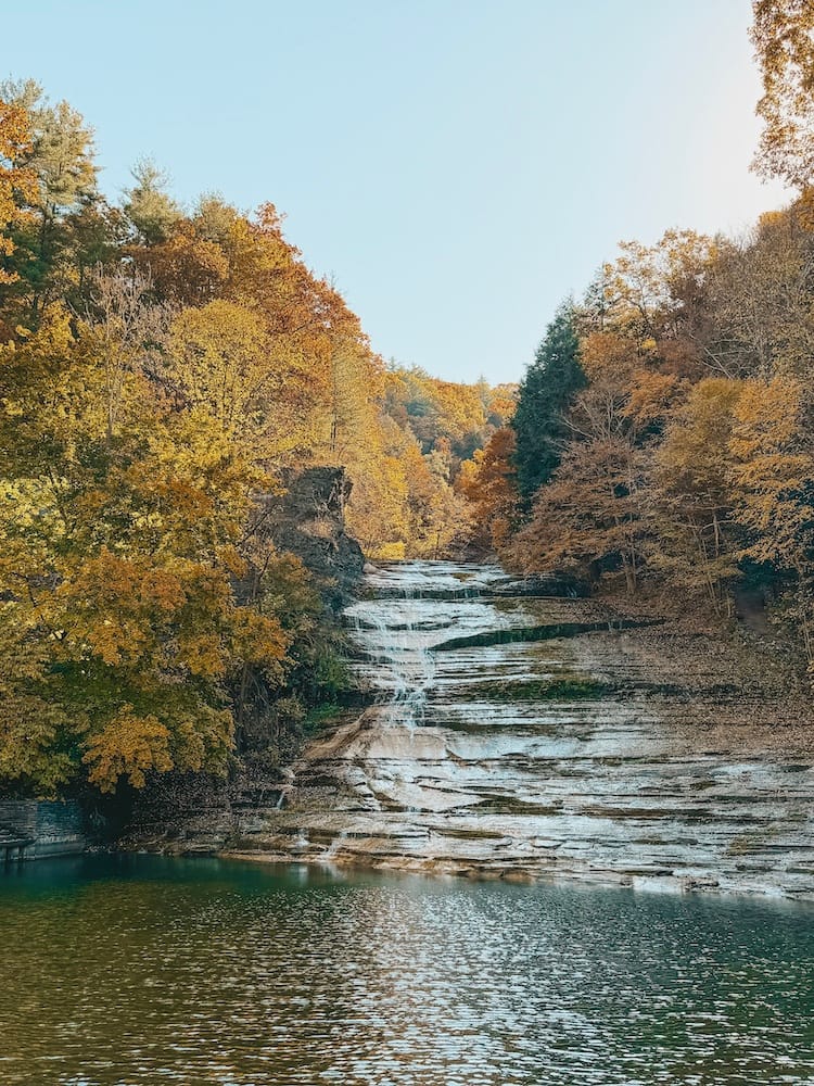 A waterfall cascading down into a pool surrounded by fall foliage