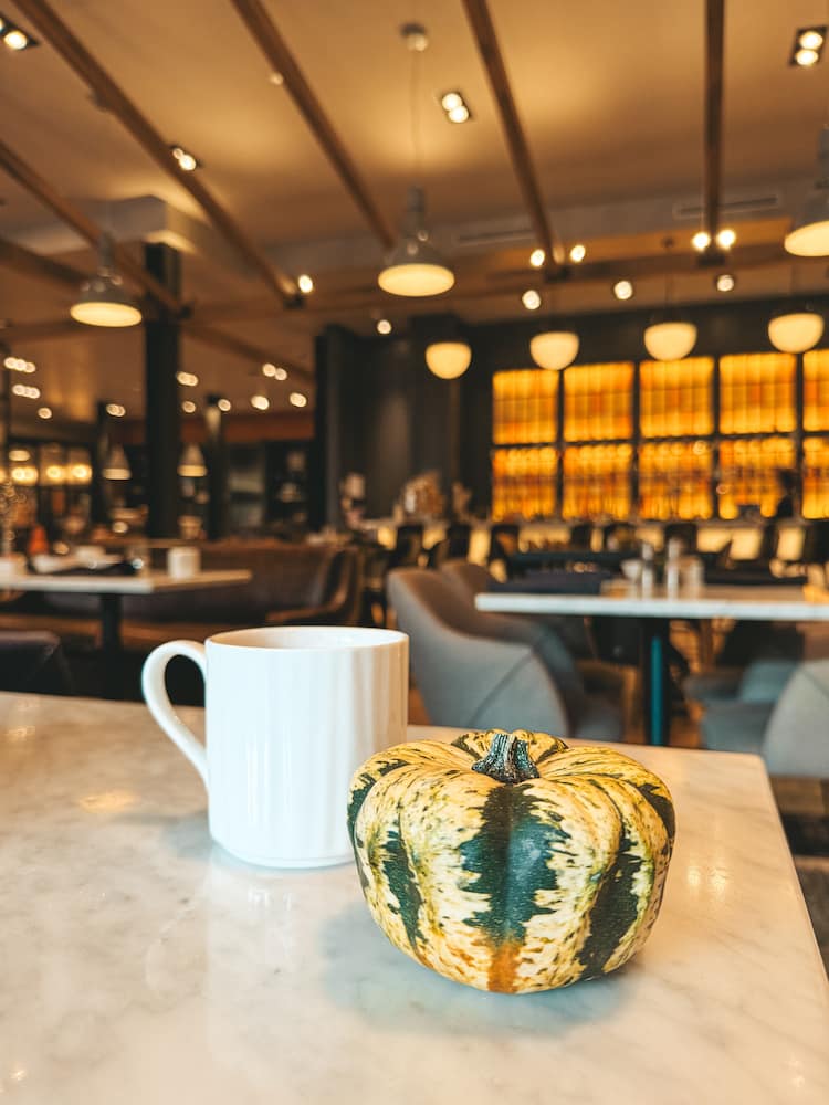 A pumpkin and a cup of coffee sitting on a table in front of a hotel lobby in Ithaca, one of the best places to stay in the Finger Lakes