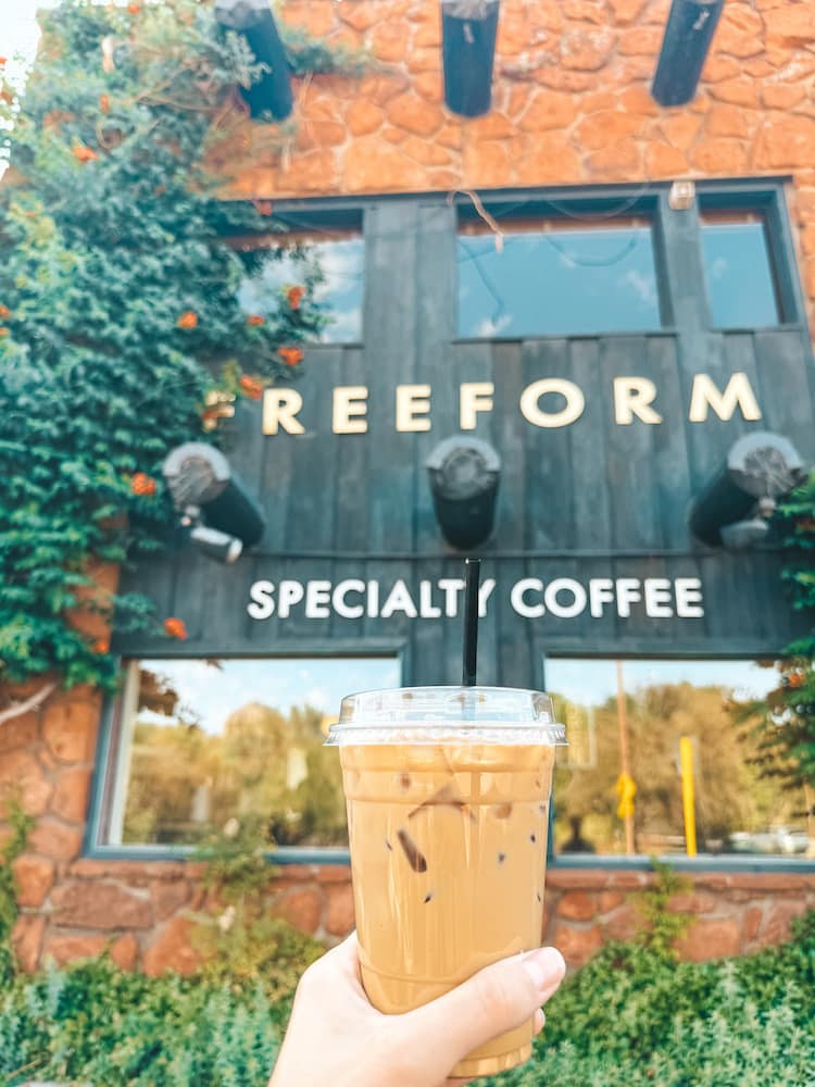 A cup of iced coffee being held up in front of the storefront for Freeform Coffee in Sedona, Arizona