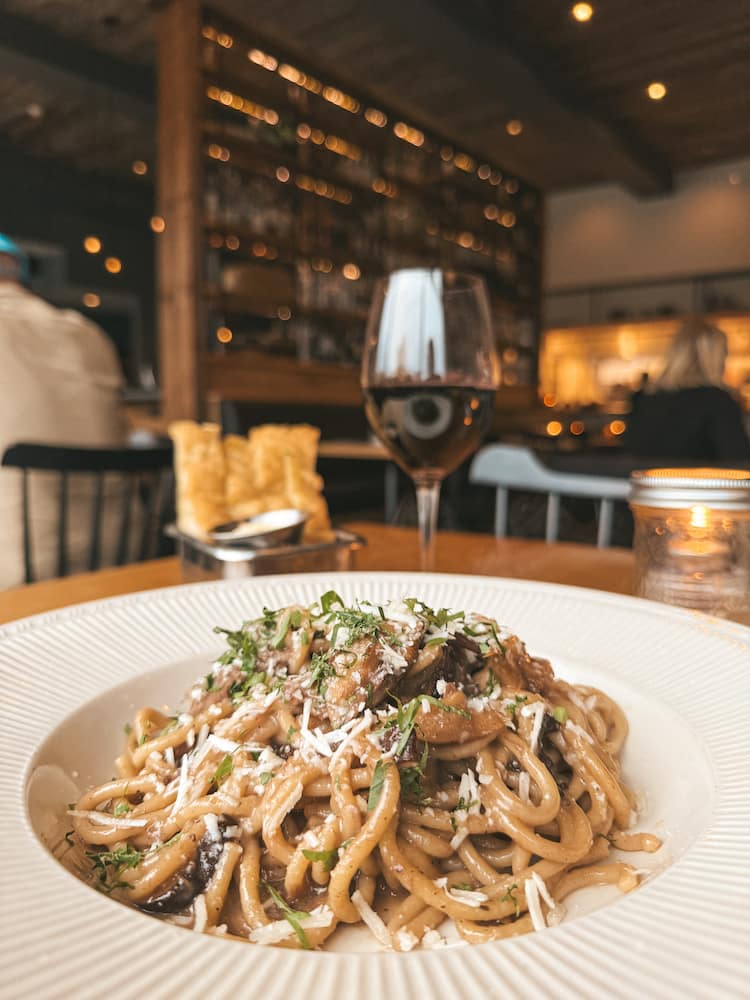 A plate of pasta sitting in front of a glass of red wine at Kindred Fare, one of the best restaurants in Geneva
