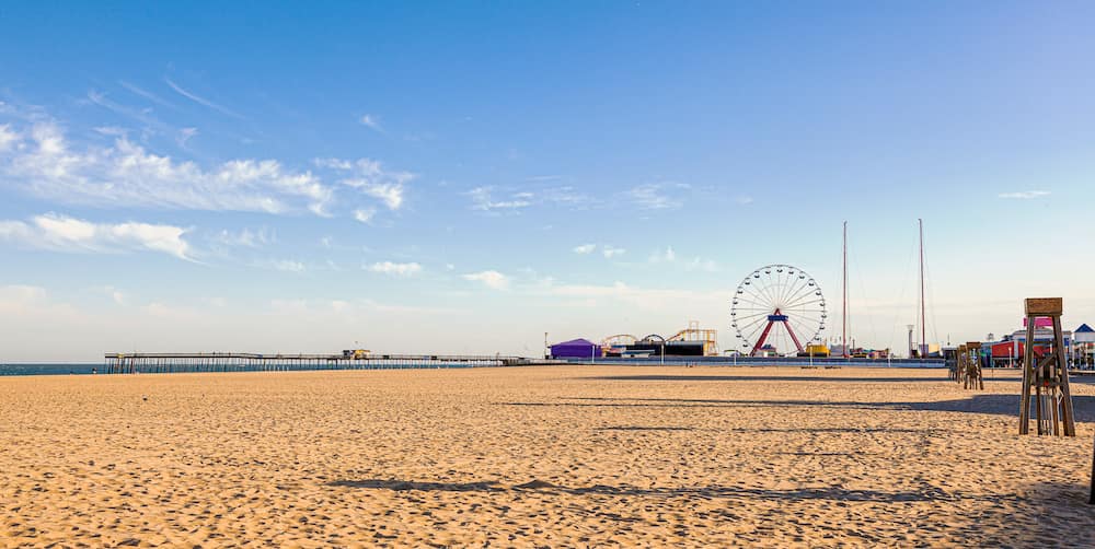 A ferris wheel, roller coaster, and other amusement park rides in the background on Ocean City Beach.