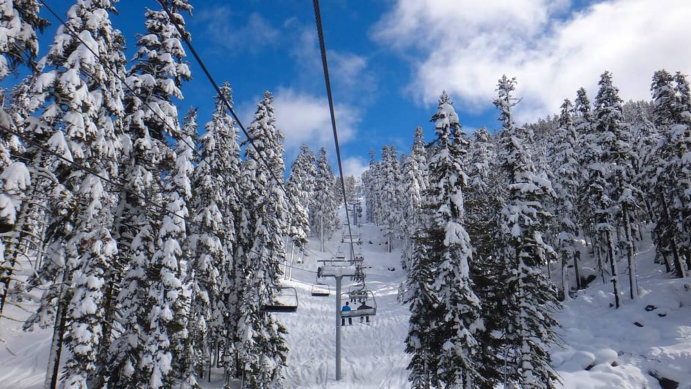 A ski lift in Lake Tahoe taking skiers up the mountain between snow-dusted trees and a blue ksy