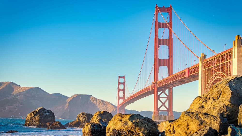 The red Golden Gate Bridge crossing over the water and tan boulders in San Francisco.