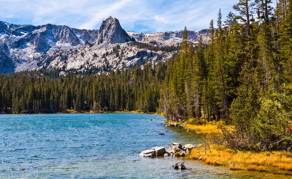 A view of the rocky mountains, green trees, yellow brush cover, and blue lake at Mammoth Lakes in California in October.