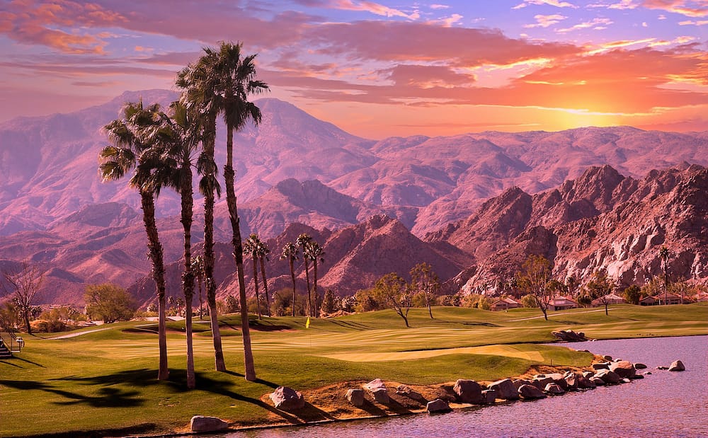 A gorgeous sunset in Palm Springs, one of the best places to visit in April in the USA, with palm trees and mountains in the background.