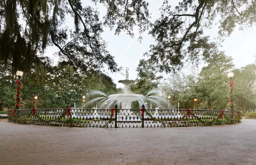 The white fountain in Forsyth Park in Savannah decorated with red bows and garland for the holidays and surrounded by mossy trees.