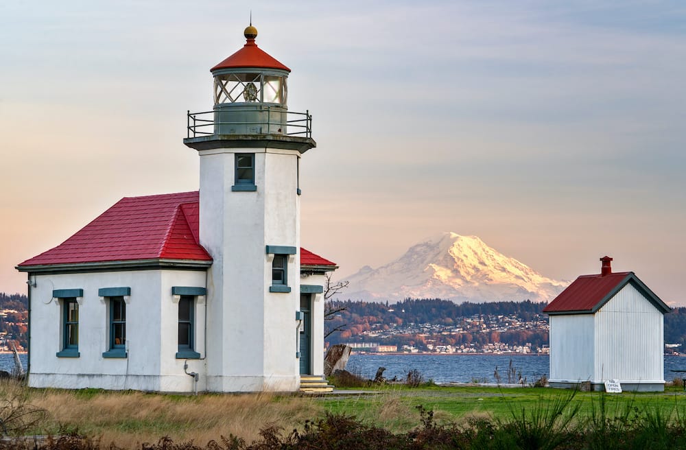 A red and white lighthouse in the foreground with Mount Ranier in the background.