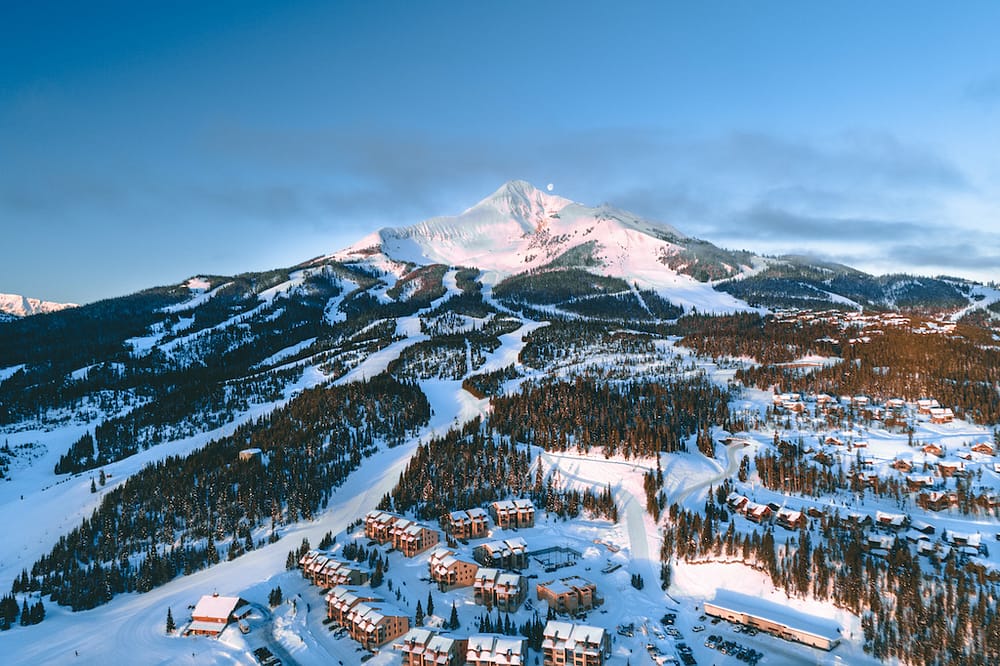 A huge snowy mountain with ski slopes running down into a ski resort in Big Sky, Montana, one of the best places to visit in the USA in February.