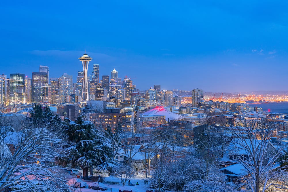 The Seattle skyline, featuring the Space Needle and other buildings with bright lights, with snow at night in the winter