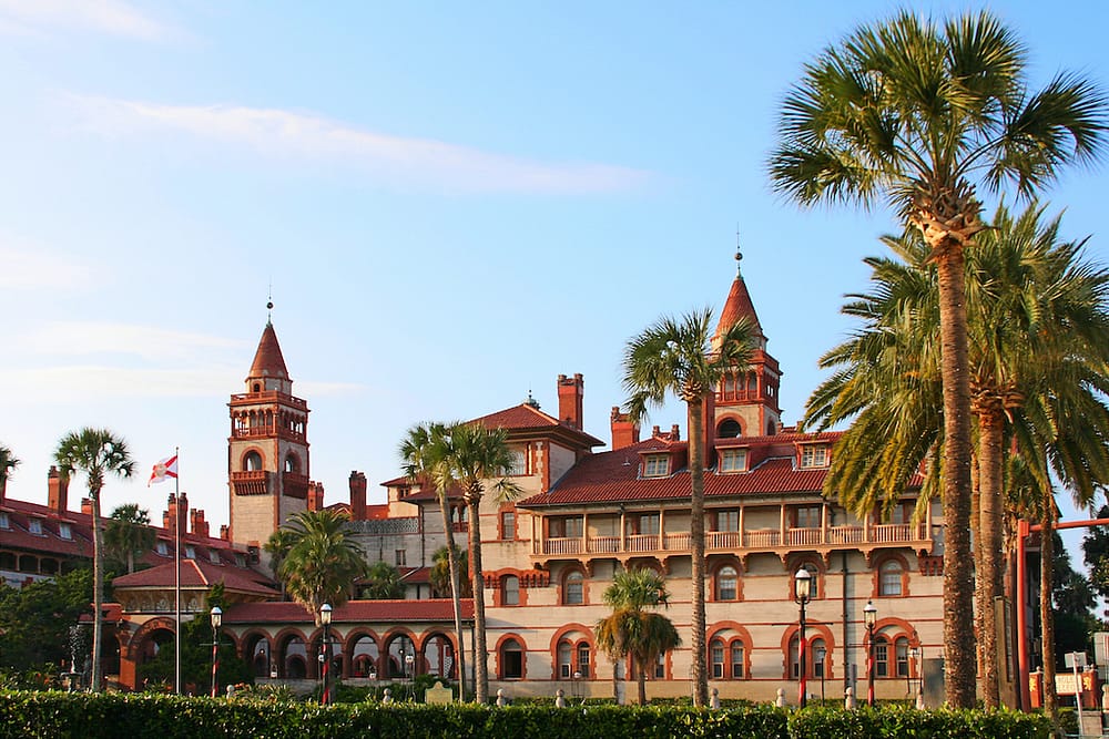 A gorgeous historic building with rust red roofing surrounded by palm trees in St. Augustine, one of the best places to vsiit in the USA in February.