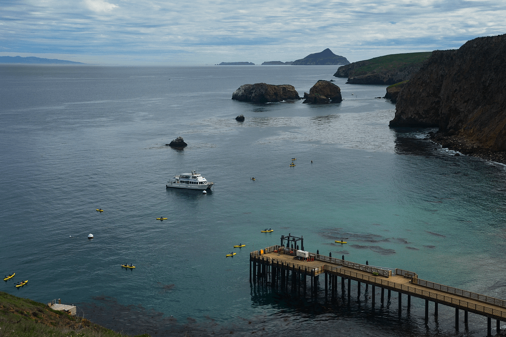 A boat and several kayaks in the water off the edge of a pier in the Channel Islands National Park