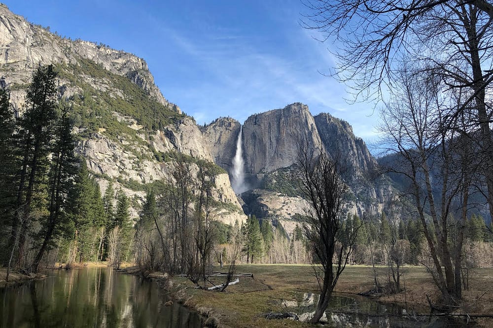 A waterfall in Yosemite National Park is surrounded by mountains and tall trees.