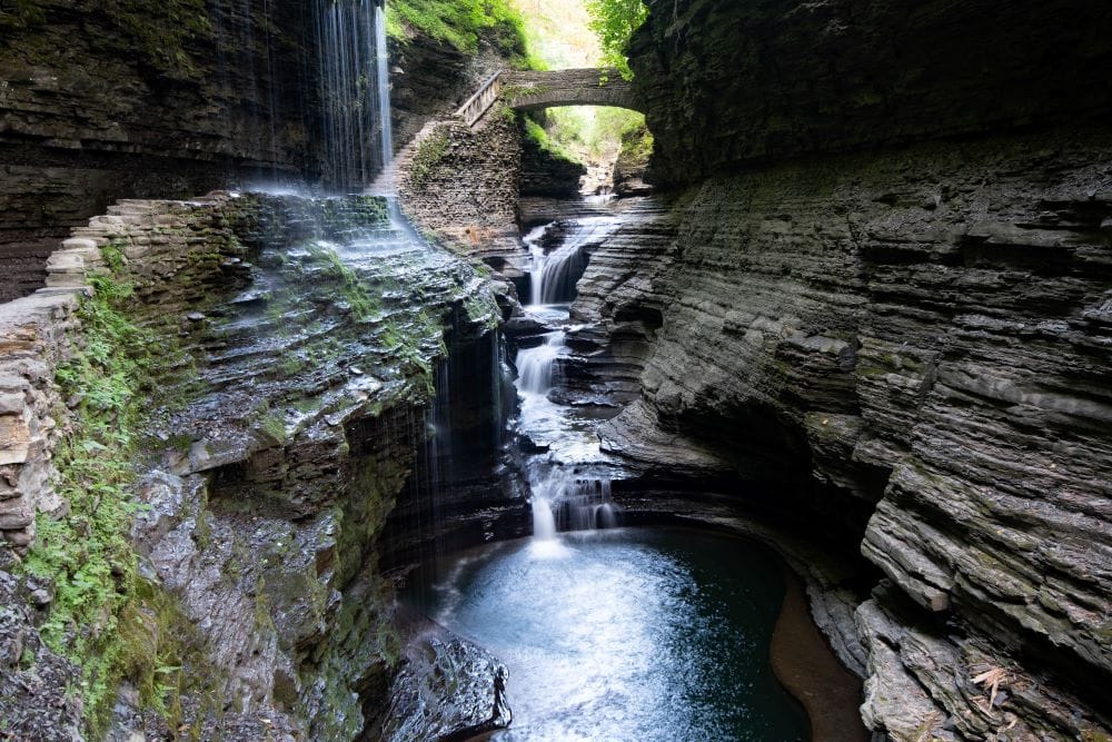 A waterfall cascading into a river in a rocky canyon on Watkins Glen State Park in New York - one of the best places to visit in May in the USA