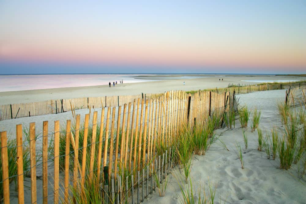 A view of the beach and a wooden gate at Cape Cod at sunset.