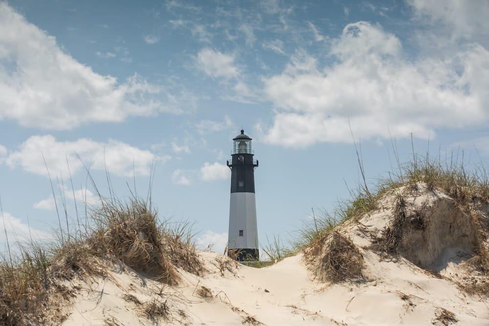 The famous black and white lighthouse at Tybee Island, one of the best summer beach vacations in the U.S., in front of some sea grass.