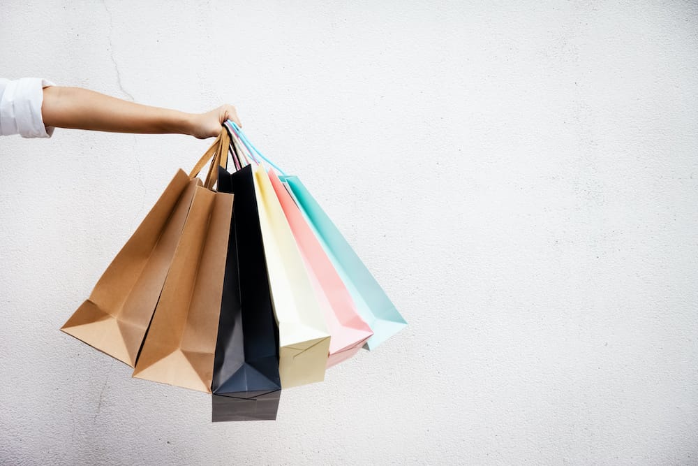 A woman holding colorful shopping bags in front of a white wall