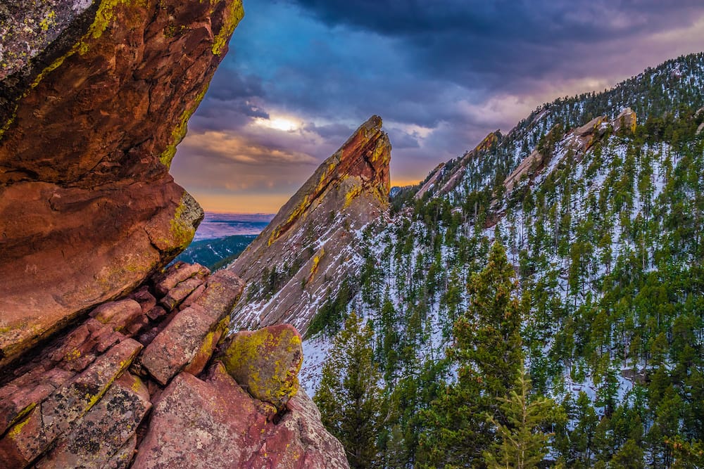 A photo of red rocks in Boulder, Colorado, dusted with trees and snow at sunset.