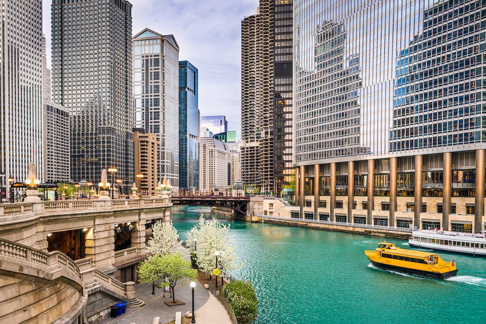 A yellow boat floating down the river that runs through the center of the skyscrapers and tall buildings in Chicago.