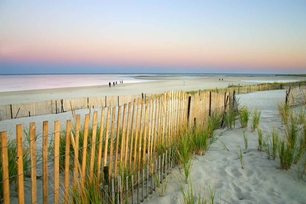 A sandy beach in Cape Cod with a wooden fence at sunset.