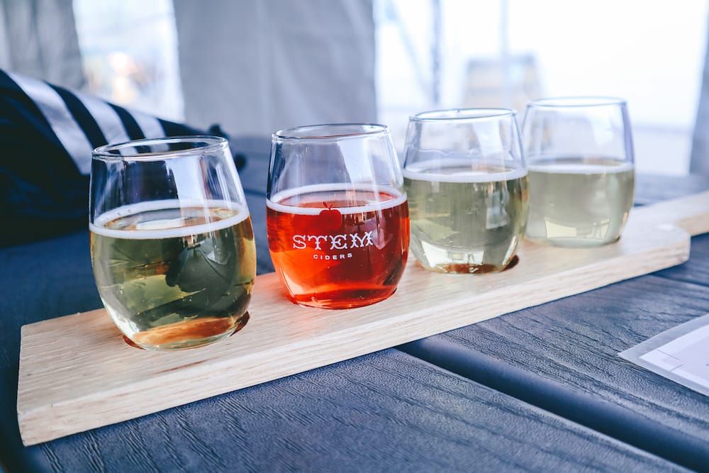 A flight of red and white ciders on a wooden table.