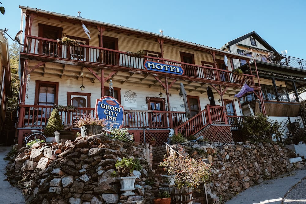 Ghost City Inn in Jerome, Arizona – a quaint two-story wood building with rock and plans out front.