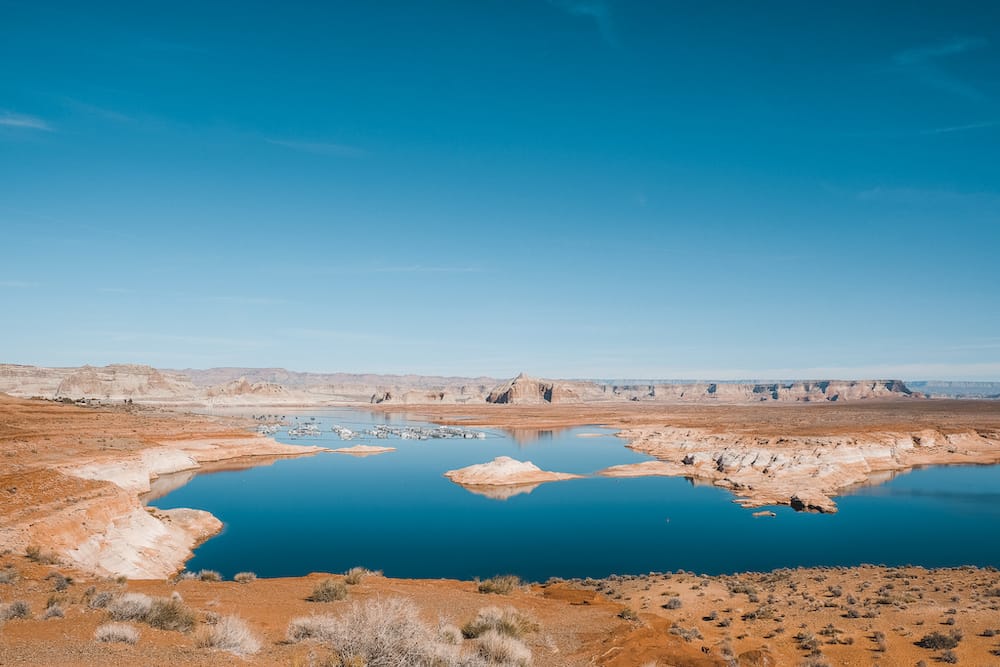 The blue water of Lake Powell surrounded by brown dirt and rock formations.