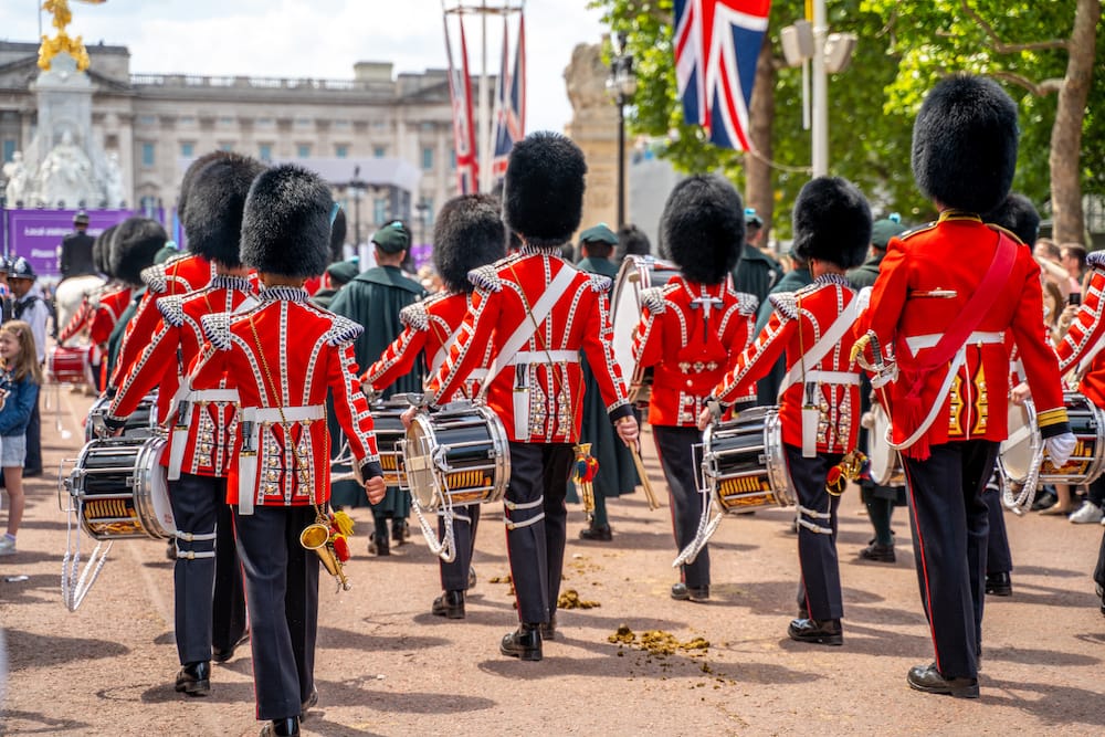 Several soldiers in red coats and black hats marching with their drums during the Changing of the Guard at Buckingham Palace – one of the best cheap things to do in London.