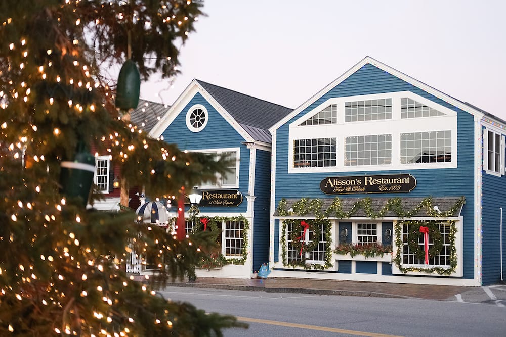 Two blue buildings in the small coastal town of Kennebunkport, Maine, decorated with greenery, red ribbons, and lights for the holidays.
