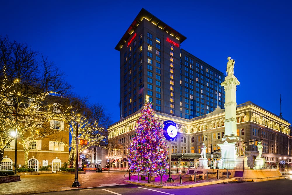 The colorful Christmas tree in Penn Square, surrounded by historic buildings and statues, and a Marriott Hotel at night.