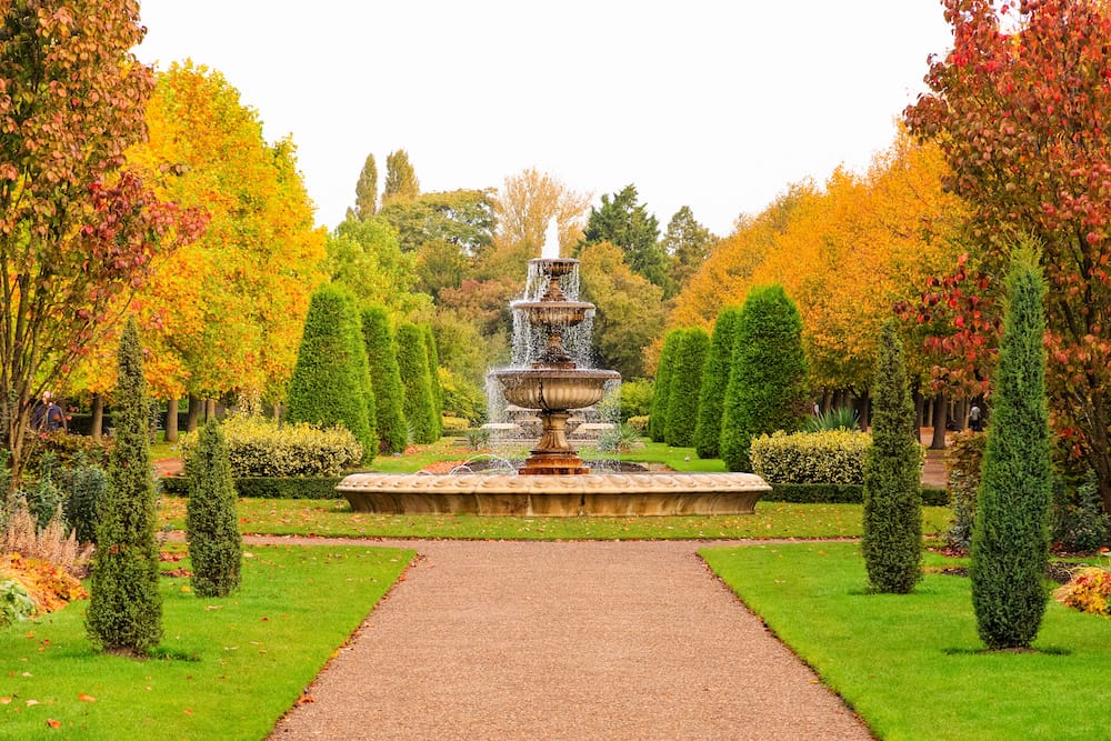 The fountain at the center of Regent's Park surrounded by yellow, green, red, and orange leaves and trees during the fall.