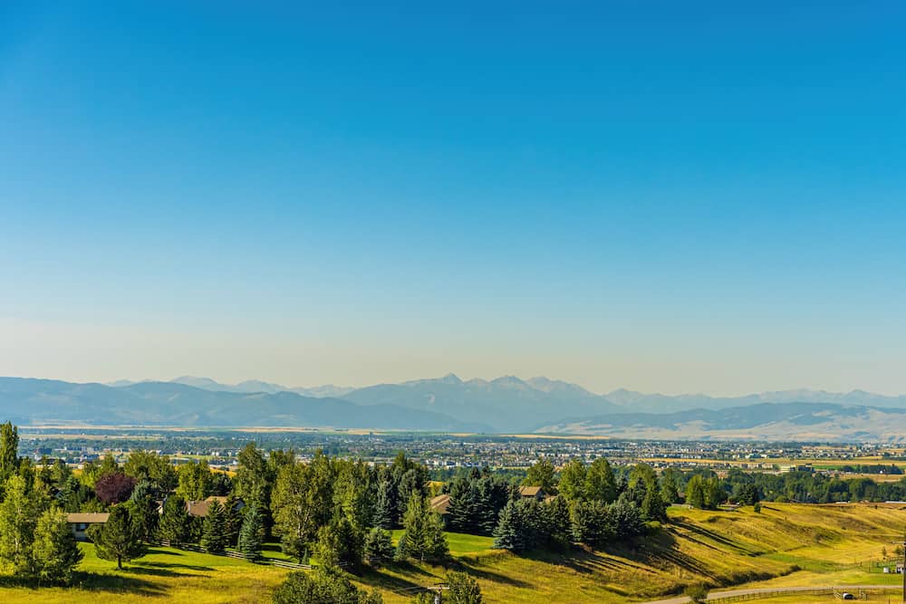 Several trees and grassy plains overlook the city and mountainous terrain in Bozeman, Montana.