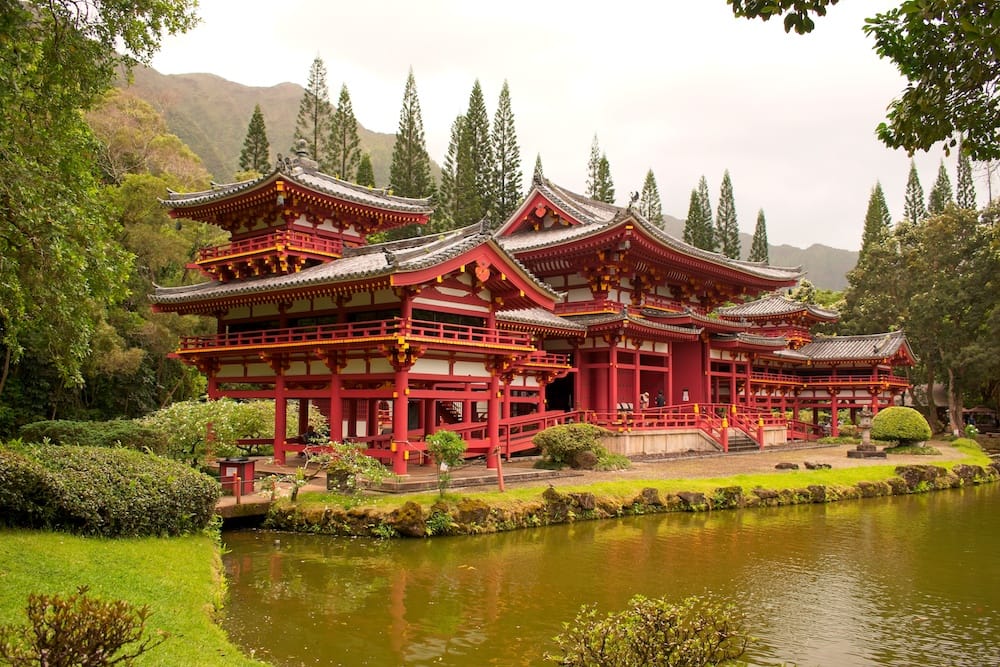The red and yellow Byodo-In Temple on Oahy surrounded by island greenery and a greenish pond.