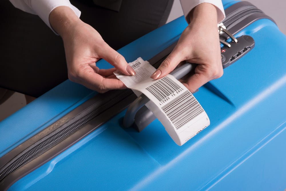 Airline check-in luggage tag being attached to a blue suitcase by the airline staff person