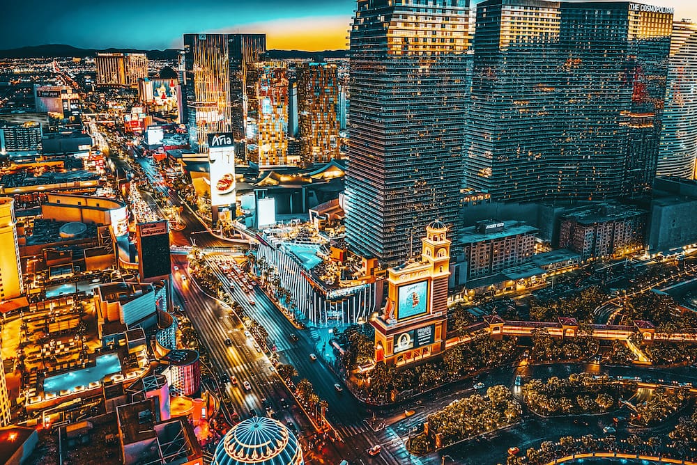 The vibrant skyline of Vegas at night from an aerial point of view, with thousands of lights, tall buildings, and people and cars present.