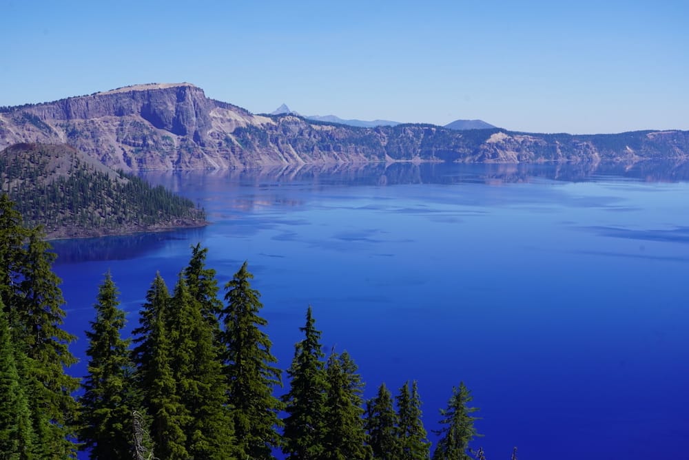 A beautiful blue lake with granite mountains in the background and green pine trees in the foreground.