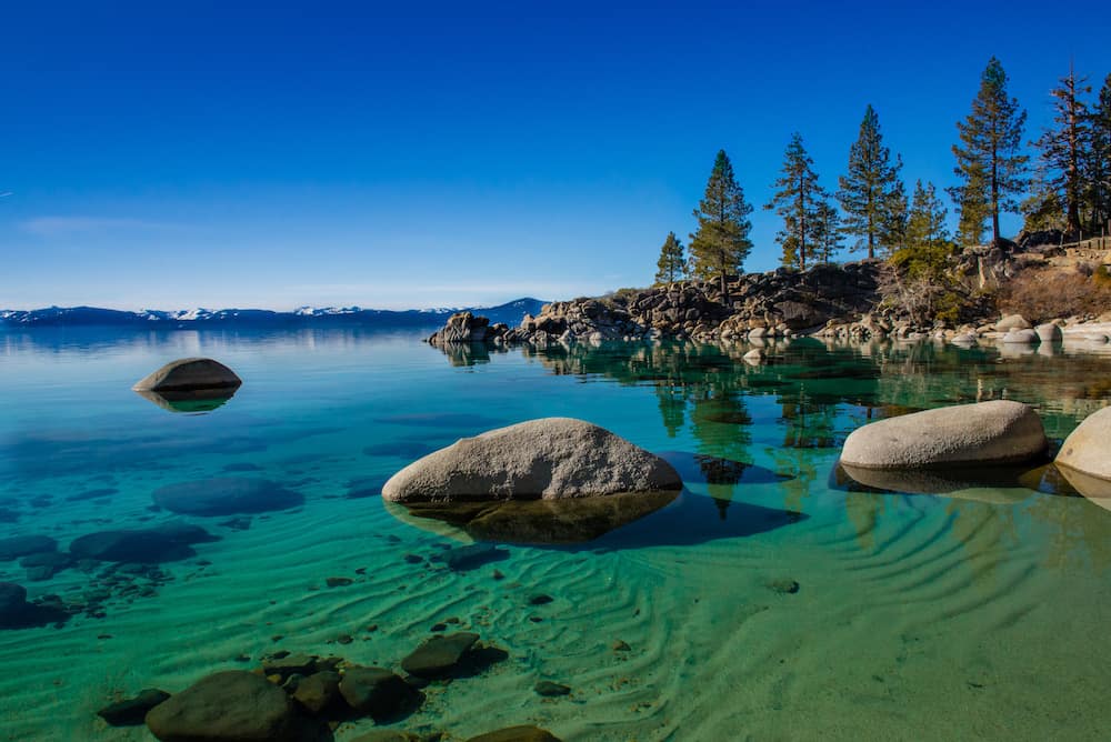 Blue water and trees and rocks in the sandy lake at Lake Tahoe