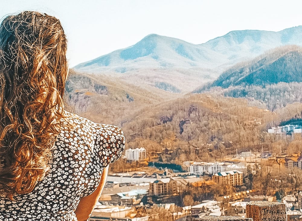A woman with long brown hair and a floral dress overlooking a small town and mountains in Pigeon Forge, one of the best day trips from Nashville.