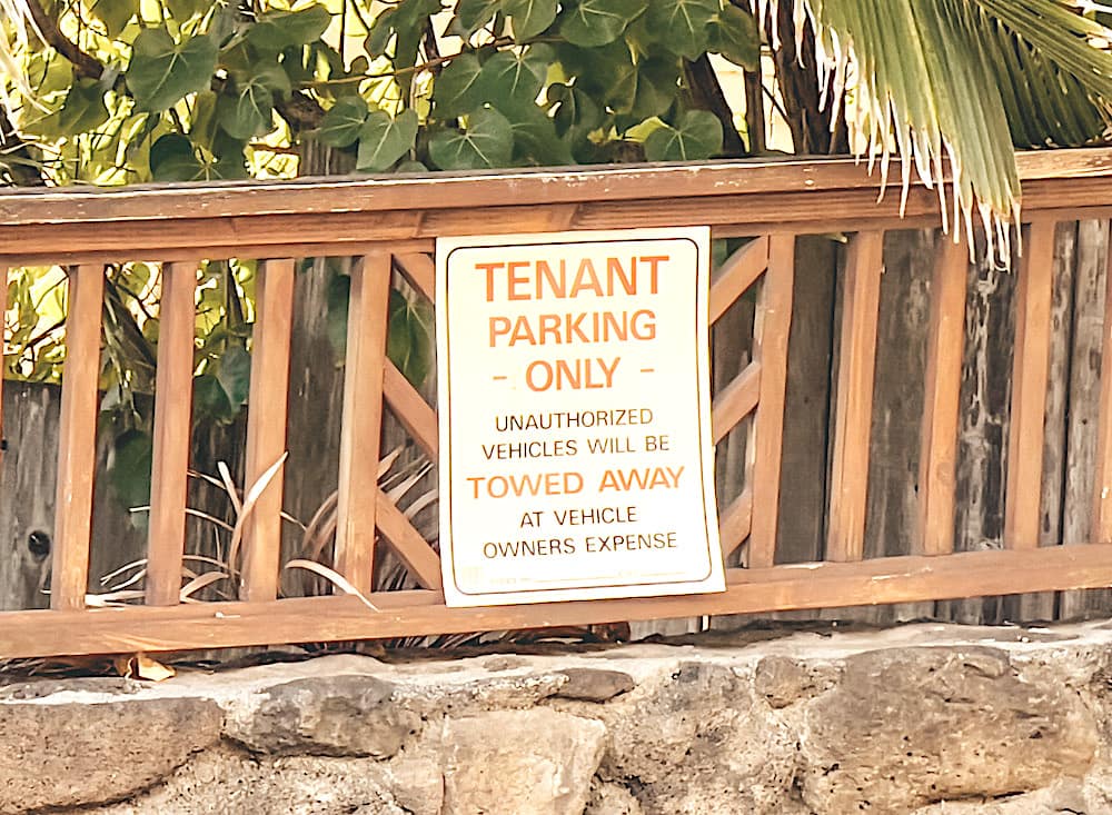 A sign that said, "Tenant Parking Only, Unauthorized vehicles will be towed away at vehicle owner expense," posted on a wooden fence above a stone wall.